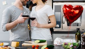 Amorous couple toasting with red wine while cooking breakfast