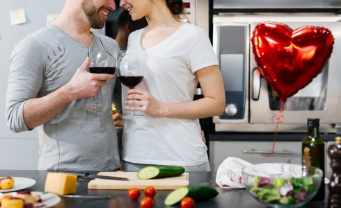 Amorous couple toasting with red wine while cooking breakfast